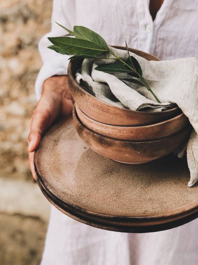 Person in white linen holding handmade ceramic bowls and plates at The Old Pottery Retreat in Thassos.